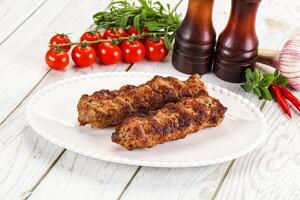 Two meat skewers on a white plate with tomatoes and spices photo
