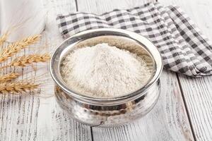A bowl of flour and a spoon next to a glass of milk photo