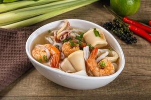 A bowl of soup with shrimp and vegetables on a table photo