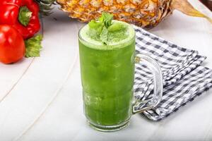 A glass of green juice next to a pineapple and other vegetables photo