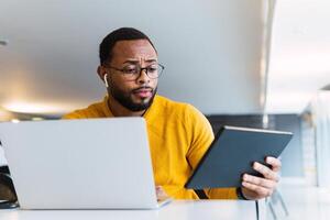 Man with earbuds using tablet and laptop at table photo