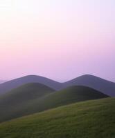A grassy hill with a pink sky and hills photo