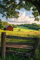 A bench sits in front of a red barn in a field photo