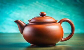A traditional Chinese teapot made of red clay stands against a turquoise wall photo