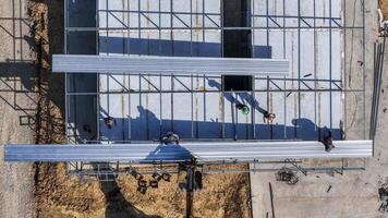 Aerial view of workers placing long metal sheets onto a building framework with the aid of heavy machinery, highlighting precision, teamwork, and modern techniques in construction projects photo