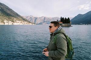 Man with a backpack stands on the seashore overlooking the island of St. George. Montenegro. Side view photo