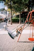 Little girl swings on a colorful swing on a playground in a park, looking to the side photo