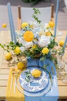 Name card lies next to an olive branch and a lemon on a plate on a set table near a colorful bouquet of flowers photo