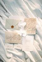 Wedding invitations and name cards lie on a white cloth sprinkled with sand photo