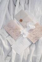 Wedding invitations with name cards lie next to envelopes and boutonnieres with beads on white fabric photo