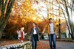 Smiling mom and dad walking with little girl holding hands on the road in the park photo