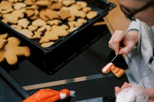Confectioner uses a toothpick to apply a pattern of icing to a cookie photo
