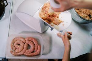 Cook stuffs the gut with minced meat on an electric meat grinder, pushing it with a pusher. Top view photo