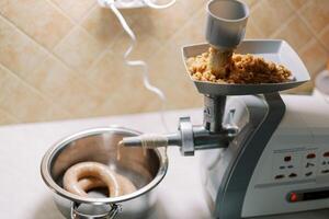 Electric meat grinder with an intestine wound on a nozzle and minced meat in the tray is on the table photo