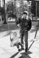 Smiling dad swings a little girl on a chain swing in the park. Black and white photo
