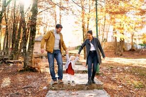 Little girl stands on a paved path in the park holding hands with mom and dad photo