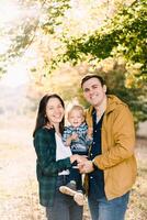 Smiling dad hugging mom with a little girl in her arms while standing in the forest photo