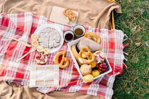 Mugs of coffee stand on a blanket next to buns and fruit in a basket and a sliced pie photo