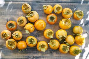 Lot of ripe persimmons lie in bulk on a wooden table. Top view photo