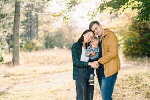Mom and dad hugging while holding their little daughter in their arms in the park photo