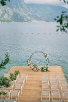 Rows of white chairs stand on the pier in front of a round wedding arch photo
