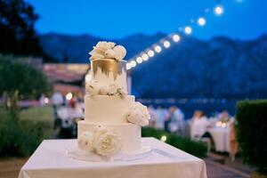 Three-tier wedding cake stands on a table in an evening garden with illumination photo