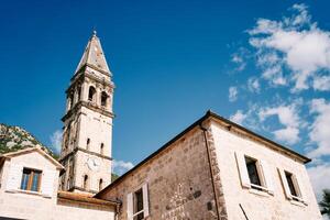 Old stone house with white shutters and an attic against the backdrop of the bell tower of the Church of St. Nicholas. Perast, Montenegro photo