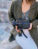 Montenegro, Tivat - July 05, 2024. Girl with a vintage Canon movie camera in her hands sits on a stone fence. Cropped photo