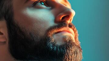 Man with beard close up eye looking up The photo is well lit with a teal and orange hue on his face and beard