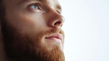 Introspective gaze of a ginger-bearded man with pale skin light blue eyes and prominent freckles against a neutral backdrop photo