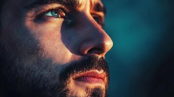 Contemplative portrait of a man illuminated by golden light gazing upwards with striking blue eyes and a thoughtful expression photo