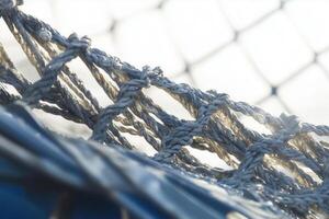 A macro shot displays the intricate knots of a durable, gray rope net against soft light. photo