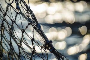 Close-up of an old fishing net with sunlit bokeh water creating a nautical atmosphere. photo