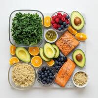 Overhead view of a nutritious meal prep featuring salmon, avocado, quinoa, kale, and fresh fruit. photo