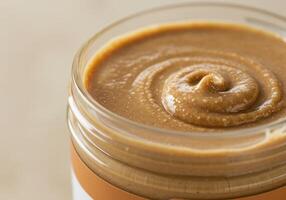 A jar of freshly made almond butter shows its creamy texture with a delectable swirl on top. photo