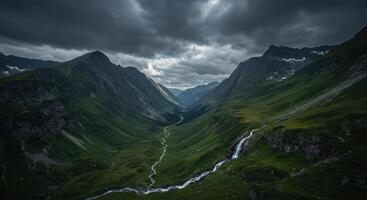 Dramatic valley featuring a cascading waterfall amidst towering mountains under a cloudy, atmospheric sky. photo