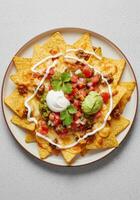 An appetizing plate of cheesy nachos is topped with ground beef, guacamole, salsa, and sour cream photo