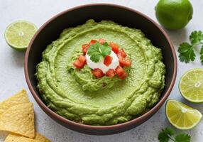 A flavorful bowl of fresh guacamole with tomatoes and cilantro is ready to be served with chips and lime. photo