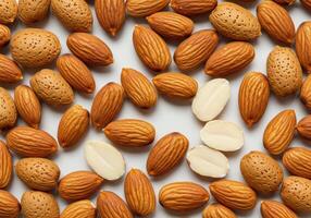 A top-down view shows a heap of raw almonds, some shelled and halved on a plain backdrop photo