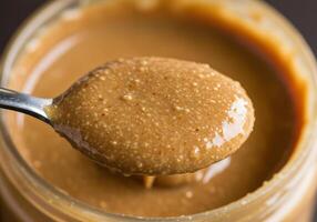 A spoonful of creamy almond butter is scooped from a jar, ready to enhance your favorite snack or breakfast. photo