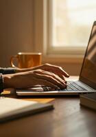 Close up of hands typing on a laptop in a warm, inviting home office setting by a window. photo