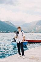 Photographer with a camera on a tripod stands on a pier by the sea and looks into the distance photo