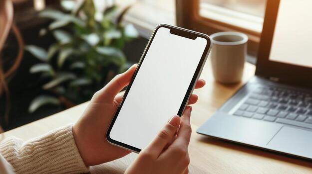 mock up phone in woman hand showing white screen, while she is working on the laptop in cafe photo