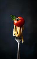 A fork with spaghetti topped with a fresh tomato and basil leaf against a dark background photo