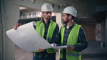 caucasiano dois pessoas homens arquitetos engenheiros rapazes machos construtores dentro capacetes capacetes e coletes discutindo construção plano projeto olhando projeto papel trabalhadores inspetor falando documento empreiteiros video
