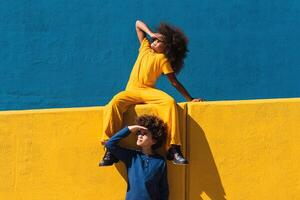 Black curly haired girl and boy resting near colorful wall photo