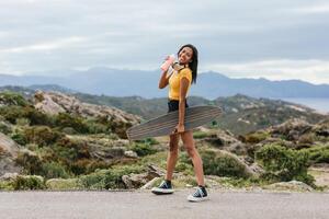 Smiling skater with longboard walking on pavement against mount photo