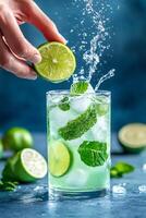 Hand squeezing a fresh lime wedge into a glass of mojito cocktail, creating a splash photo