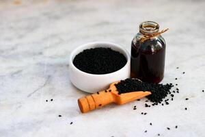 Sesame oil in a small bottle and black sesame seeds in a wooden spoon photo