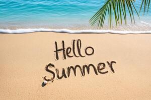 Hello summer written on beach sand with palm tree leaf and turquoise water photo